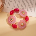 Detalle de anillos de acrílico rosa y cuentas rojas irregulares sobre página de libro - Pulsera / Rosa