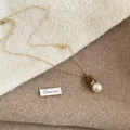 Detail van een ketting met een beertje en parel op een gezellige gebreide achtergrond - Bruine beer boog parelketting (12#)