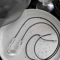 Ciondolo a U irregolare in argento su cordoncino nero, presentato su un vassoio di ceramica - Cordino Nero - Ciondolo Argentato / Nero/Argento