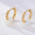 Close-up of golden hoop earrings with translucent white stone on a stone background - Opal