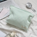 Detail of green plaid makeup bag with woven label on a white bed linen background - Wrinkled Green Plaid