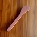 Pink plastic skincare spatula and cosmetic mixing tool on dark wood background - Solid Pink
