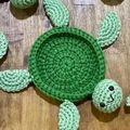 Handmade crochet turtle coaster in dark green yarn on wooden table surface - Aqua & Emerald Green