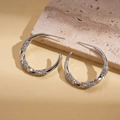 Macro shot of silver C-shaped twisted hoop earrings with pave-set zircons on beige leather - Real Gold Plated / Silver Pin - Silver - Medium
