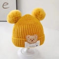 Detail of yellow knitted baby hat with twin pom-poms and a cute cartoon bear patch - Double Pompom LUCK Bear Yellow