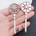 Detail view of two antique silver key pendants with floral hollow patterns held by hand - Round Pattern Key (7522)