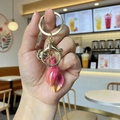Pink gradient shell keychain with golden bell and metal clip accessory on hand - Small Yellow Conch