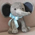 Gray plush elephant toy with light blue ribbon bow on a soft beige sofa background - Grey With Blue Ribbon