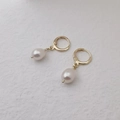 Elegant gold hoop earrings with white teardrop pearls on a textured background - Earrings