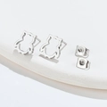 Detailed view of silver owl-shaped stud earrings with hollow design on a white plate - Owl / Steel