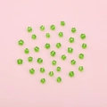 DIY handmade green flower-shaped glass beads for jewelry making on pink background - Green