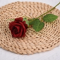 Single dark red artificial rose flower with green leaves on a woven straw mat decoration - Burgundy