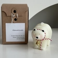 Polar bear scented candle in white with red ribbon and bells next to kraft gift box - White Blushed Polar Bear with Bell
