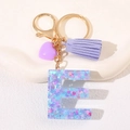 Macro view of a resin letter E keychain with purple tassels and glitter star accents - Letter E