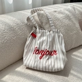 Détail de la broderie rouge 'bonjour' sur un sac cabas en toile rayée posé sur un canapé - Blanc