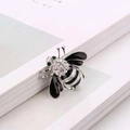 Silver bee brooch with black enamel wings and sparkling rhinestones on a magazine page - Silver Black Enamel Bee