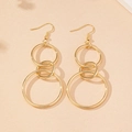 Detailansicht modischer, dreifach verbundener goldener Ringohrringe auf beigefarbener Fläche - Gold