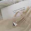 Dettaglio di un ciondolo a cuore in argento con zirconi su un sacchetto in tessuto beige - Argento 925 / Argento