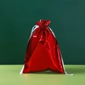 Metallic red drawstring gift bag with elegant white ribbon closure on a green surface - 29*43cm Laser Flame Red