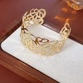 Detailopname van een gouden cuff-armband met fijn roosvormig opengewerkt patroon - Goud