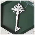 Close-up of vintage resin key ornament with white silk ribbon in a dark green tray - Key-Ivory White