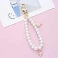Close-up of pearl keychain with white lollipop and flower charms on pink background - Lollipop Pearl Chain