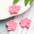 Macro shot of three pink resin cherry blossom charms with yellow stamens on ceramic plate - Rose Red