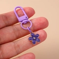 Detailed close-up of a purple flower keychain charm with golden center held by hand - Purple Flower