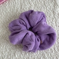 Close-up of a purple towel fabric hair scrunchie with a round metal tag on white knit - Scrunchie / Purple