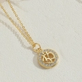 Detailansicht eines goldenen Om-Anhängers mit Zirkonia-Lünette auf Lederhintergrund - Om Symbol