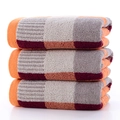 Three stacked cotton face towels featuring a warm orange and grey checkered plaid pattern - Color Block Grid - Orange
