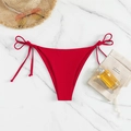Detail of red tie-side bikini bottoms on marble background with vacation accessories - Red