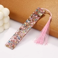 Macro detail of a clear acrylic bookmark with colorful foil flakes and a pink tassel - Pink