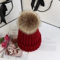 Detail shot of a thick red knitted beanie with a large light brown faux fur pompom - Adult One Size 56-58cm / Burgundy