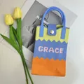 Detail of knitted phone bag with wave patterns and Grace embroidery on a white surface - Color Block Yellow-Grace