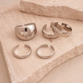 Detalle de cinco anillos ajustables de plata pulida sobre un pedestal de piedra beige - Set de 5 piezas / Plateado