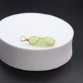 Green jade hexagonal pendant wrapped in gold wire on a white stand with black background - Luminous