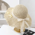 Dettaglio cappello di paglia con fiocco di pizzo bianco e accento giallo su supporto oro - Beige