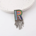 Close-up of R-shaped brooch with rainbow embroidery, rhinestones and tassel detail - Letter R