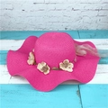 Détail d'un chapeau en paille fuchsia avec fleurs beige et large bord ondulé chic - Rose rouge