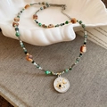 Detalle de collar de cuentas con colgante de luna y estrella en bandeja de caracol - Plata/Verde/Café