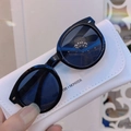 Detail of round black children's sunglasses on a white portable gallery carry case - Black Frame Grey Lens