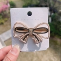 Fermaglio a fiocco dorato con perle e strass colorati tenuto in mano all'aperto - Fiocco di Perle
