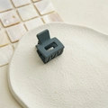Detailed view of a small matte grey-green square hair claw clip on a beige ceramic plate - Olive Green