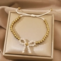 Elegant gold beaded bracelet featuring a white bow charm and adjustable woven cord - Gold Bead White Bow Bolo Bracelet (N-1110)
