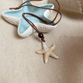 Collar con colgante de estrella de mar con cordón marrón sobre plato de cerámica azul - Estilo de Cuentas de Madera y Cuero con Estrella de Mar de Acrílico