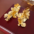 Makroaufnahme goldener Metallblumen-Ohrringe auf einer Vintage-Holzkiste mit 3D-Blüten - Goldene Blume