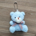 Close-up of blue curly plush bear keychain with checkered bow on wooden background - Blue