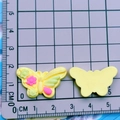 Detailed view of yellow resin butterfly charms with size measurements on a grid mat - Yellow