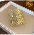 Top view of gold wide cuff bracelet with cutout floral patterns on a beige jewelry tray - Hollow Flower Bracelet / Bracelet-Gold